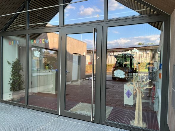 Kindergarten Sausewind Eine gläserne Eingangstür die von innen mit dem Wort Sausewind beklebt ist.