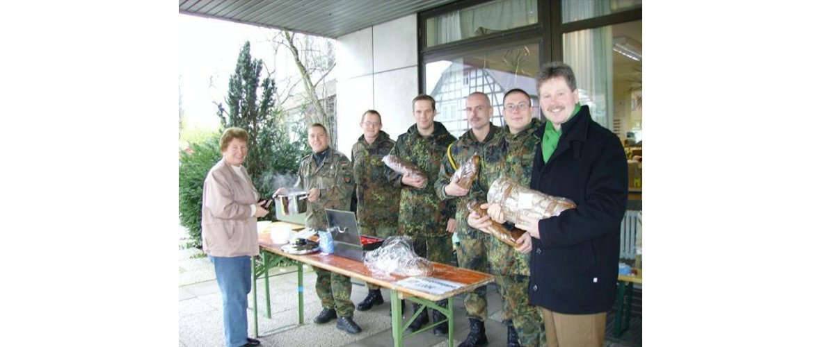 Fabian Keil (2. von links) übergibt Frau Gertrud Lukes die wohlschmeckende Suppe. Bürgermeister Klemens Olbrich (rechts), Hauptfeldwebel Oliver Zyskowski (3. von rechts) und Oberleutnant Torben Meins (4. von rechts) freuen sich mit allen Beteiligten über die gute Resonanz der Aktion.