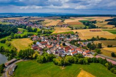 Luftaufnahme Rückershausen Luftaufnahme des Stadtteils Riebelsdorf im Sommer. Im Vordergrund links ist ein Teil eines Teichs mit einer Scheune zusehen rechts daneben eine große Wiese. Im Hintergrund links sieht man Riebelsdorf, rechts im Hintergrund eine Hügellandschaft. Der Himmel ist teils bedeckt.