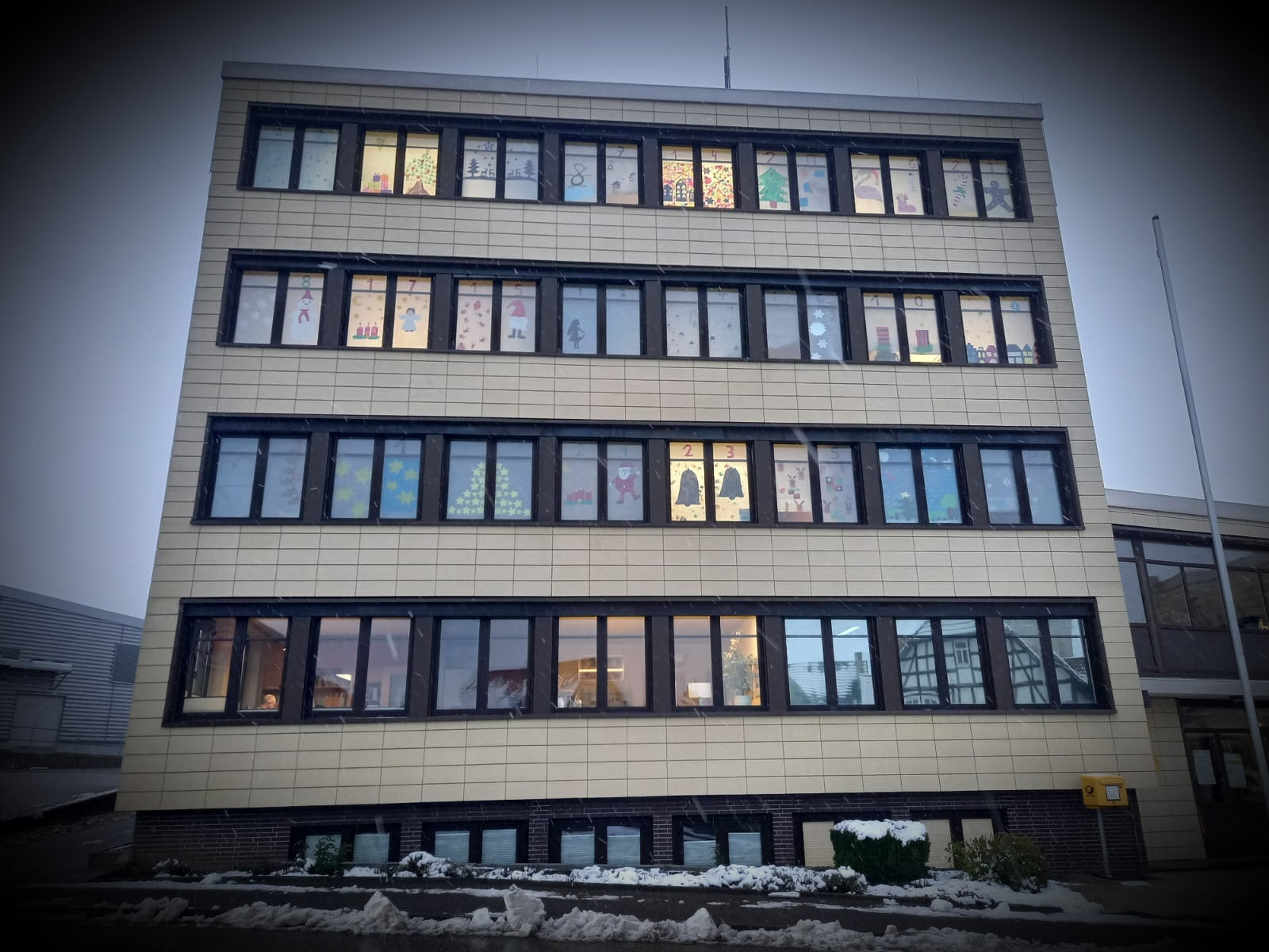 Das Rathaus der Stadt Neukirchen mit beleuchteten Fenstern die mit den von Kindergartenkindern gebastelten Bildern beklebt sind. 