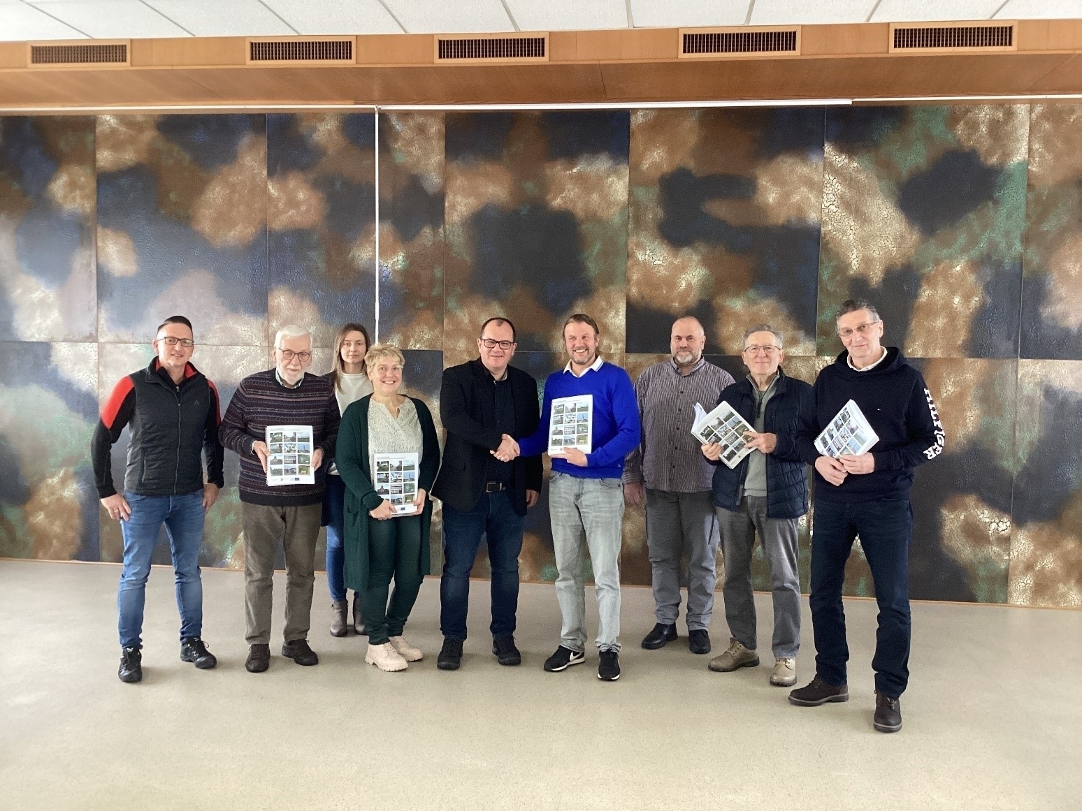 Die IKEK Steuerungsgruppe von links Thorsten Brill (Steuerungsgruppe), Helmut Reich (Steuerungsgruppe), Ljuba Iljin (Sachbearbeiterin), Nicole Mattheis (Steuerungsgruppe), Bürgermeister Marian Knauff, Marco Link (Arbeitsgruppe Stadt), Sven Hübl (Steuerungsgruppe), Willi Berg (Steuerungsgruppe), Hartwig Hepp (Steuerungsgruppe) steht im Stadtverordnetensitzungssaal der Stadt Neukirchen. Einige Steuerungsmitglieder halten das Stadtentwicklungskonzept in der Hand.