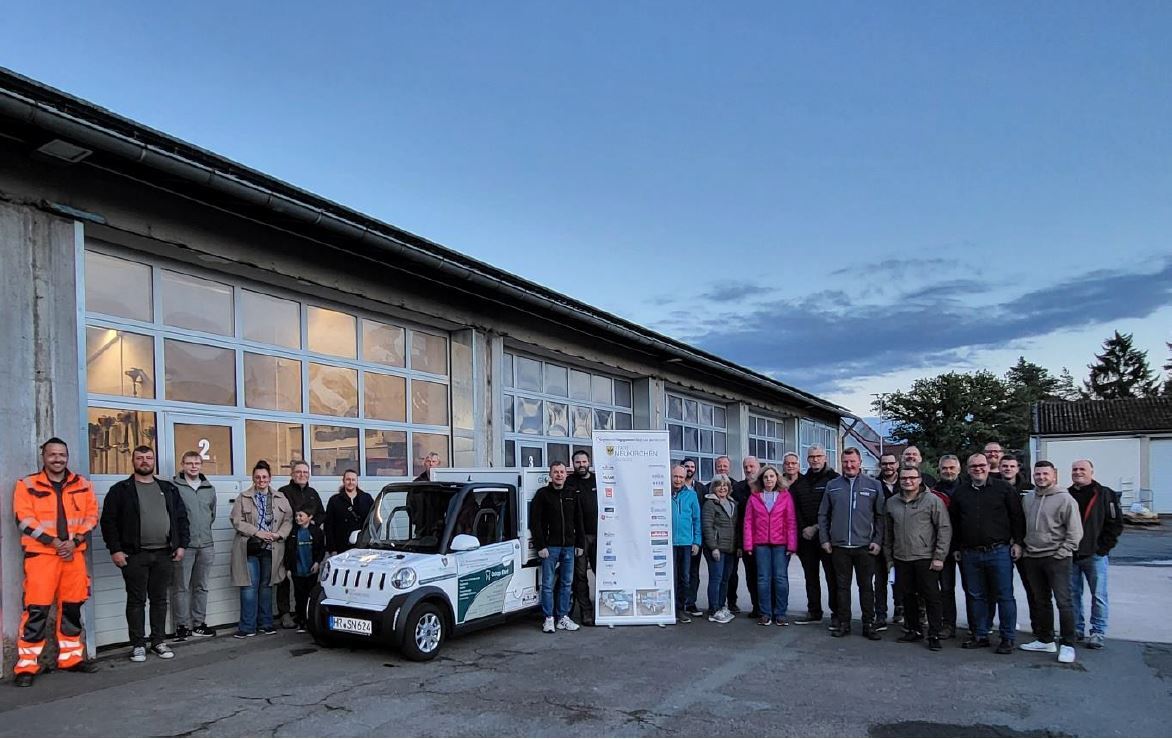 Auf dem Bild sehen wir einen Teil der Geschäftsleute, die dieses Fahrzeug mit ihrer Werbung finanziert haben sowie den Fahrzeugwart Eckhardt Berg, einige Betriebskommissionsmitglieder, den Eigenbetriebsleiter Günter Schmitt und Bürgermeister Marian Knauff. Im Hintergrund befinden sich mehrere Tore des städtischen Bauhofes. 