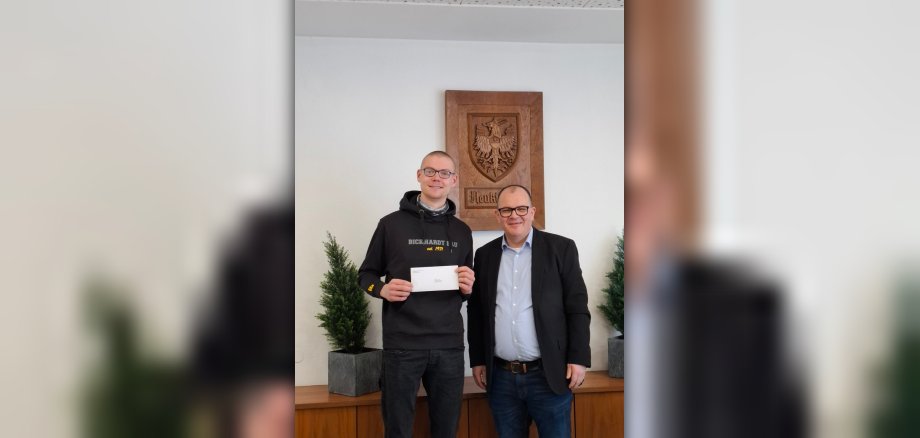 Im Magistratszimmer des Rathauses Neukirchen stehen vor dem Stadtwappen der Deutsche Meister im Straßenbau Aaron Schäfer und Bürgermeister Marian Knauff