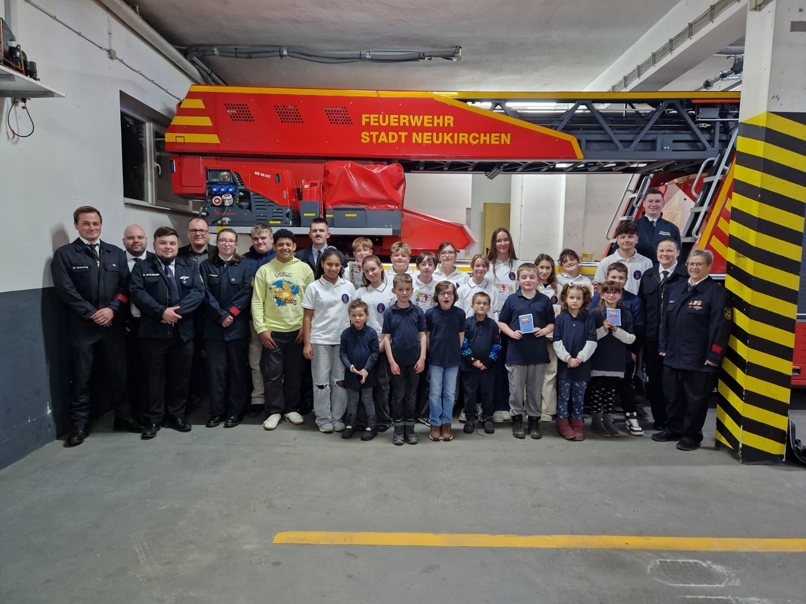 Vor dem Drehleiter-Einsatzfahrzeug im Feuerwehrhaus Neukirchen stehen die Mitglieder der Kinder- und Jugendfeuerwehrabteilung der Stadt Neukirchen mit ihren Betreuerinnen und Betreuern gemeinsam mit dem Wehrführer, dem Stadtjugendfeuerwehrwart und dem Bürgermeister.