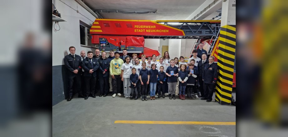 Vor dem Drehleiter-Einsatzfahrzeug im Feuerwehrhaus Neukirchen stehen die Mitglieder der Kinder- und Jugendfeuerwehrabteilung der Stadt Neukirchen mit ihren Betreuerinnen und Betreuern gemeinsam mit dem Wehrführer, dem Stadtjugendfeuerwehrwart und dem Bürgermeister.