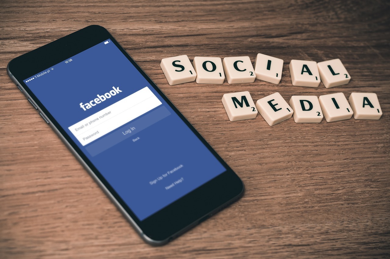 Auf dem Bild ist ein Smartphone zu sehen - es liegt auf einem Tisch. Daneben sind mit kleinen Buchstabensteinchen die Worte "Social Media" gelegt