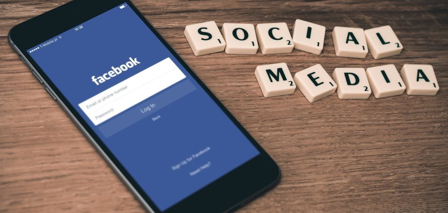 Auf dem Bild ist ein Smartphone zu sehen - es liegt auf einem Tisch. Daneben sind mit kleinen Buchstabensteinchen die Worte "Social Media" gelegt