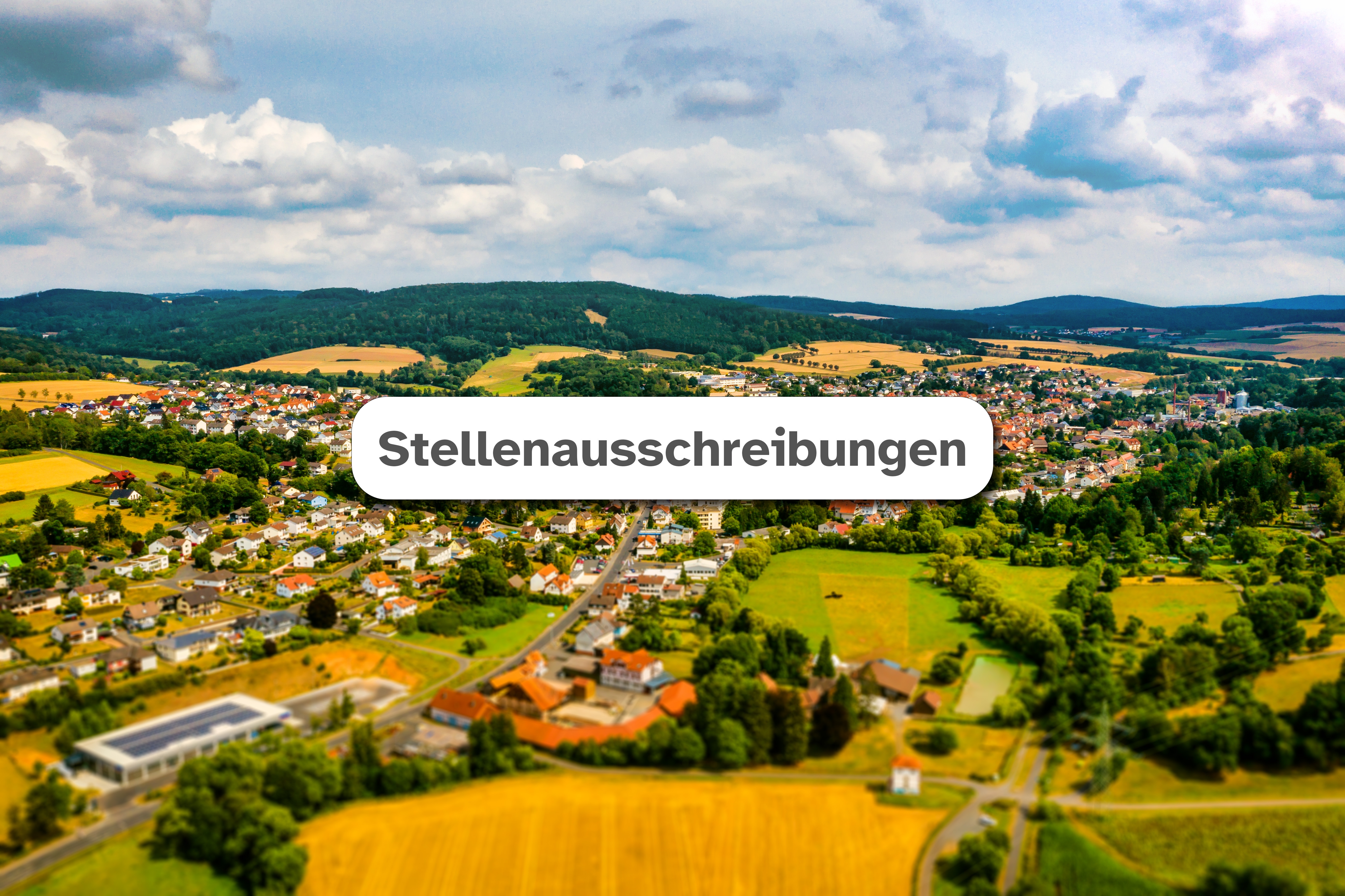 Luftaufnahme der Stadt Neukirchen im Hintergrund mit weißem Feld mittig in dem der Text "Stellenausschreibungen" zu lesen ist.