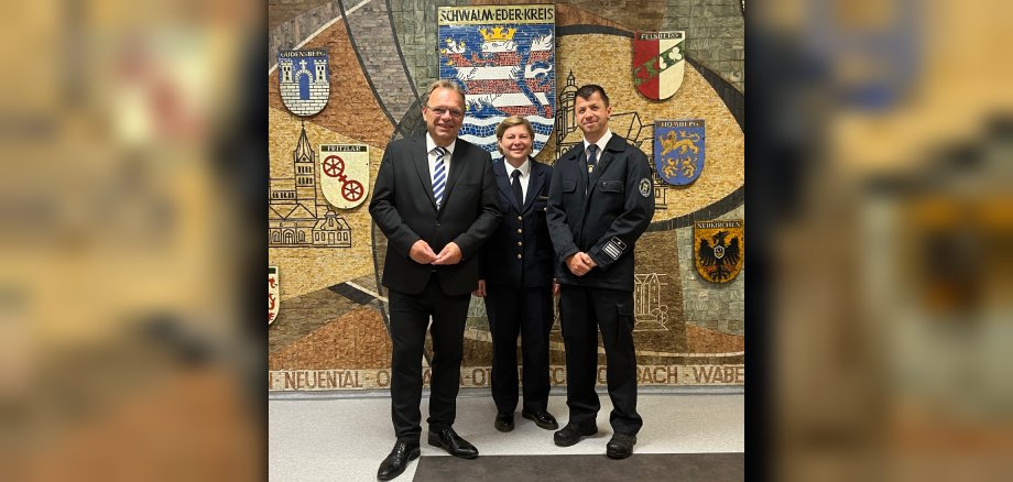 Auf dem Bild stehen (v.l.n.r) Landrat Winfried Becker, Frau Tanja Dittmar und Matthias Poppitz vor dem Wappen des Schwalm-Eder-Kreises.