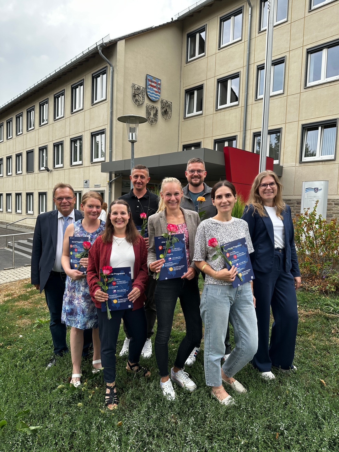 Auf dem Foto ist eine Gruppe von 6 Absolventinnen und Absolventen zu sehen mit Zertifikat und Blume in der Hand. Am Rand stehen Landrat Becker und Frau Preißner von er vhs.