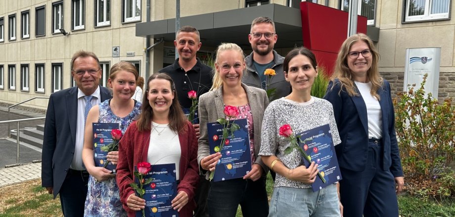 Auf dem Foto ist eine Gruppe von 6 Absolventinnen und Absolventen zu sehen mit Zertifikat und Blume in der Hand. Am Rand stehen Landrat Becker und Frau Preißner von er vhs.