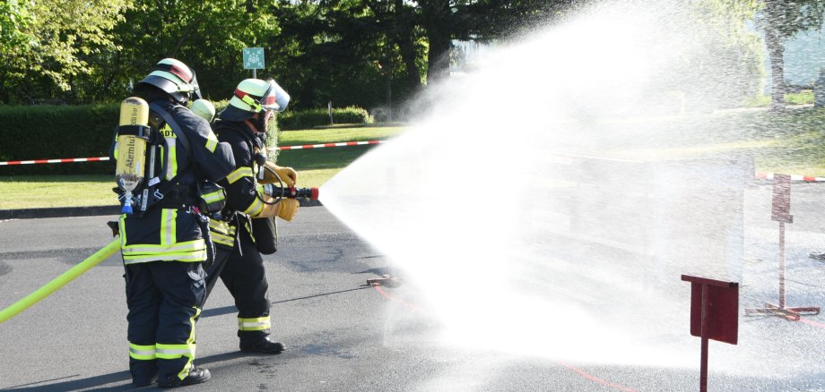 Auf dem Foto sind zwei Feuerwehrleute zu sehen, die einen Wasserschlauch halten aus dem Wasser spritzt.