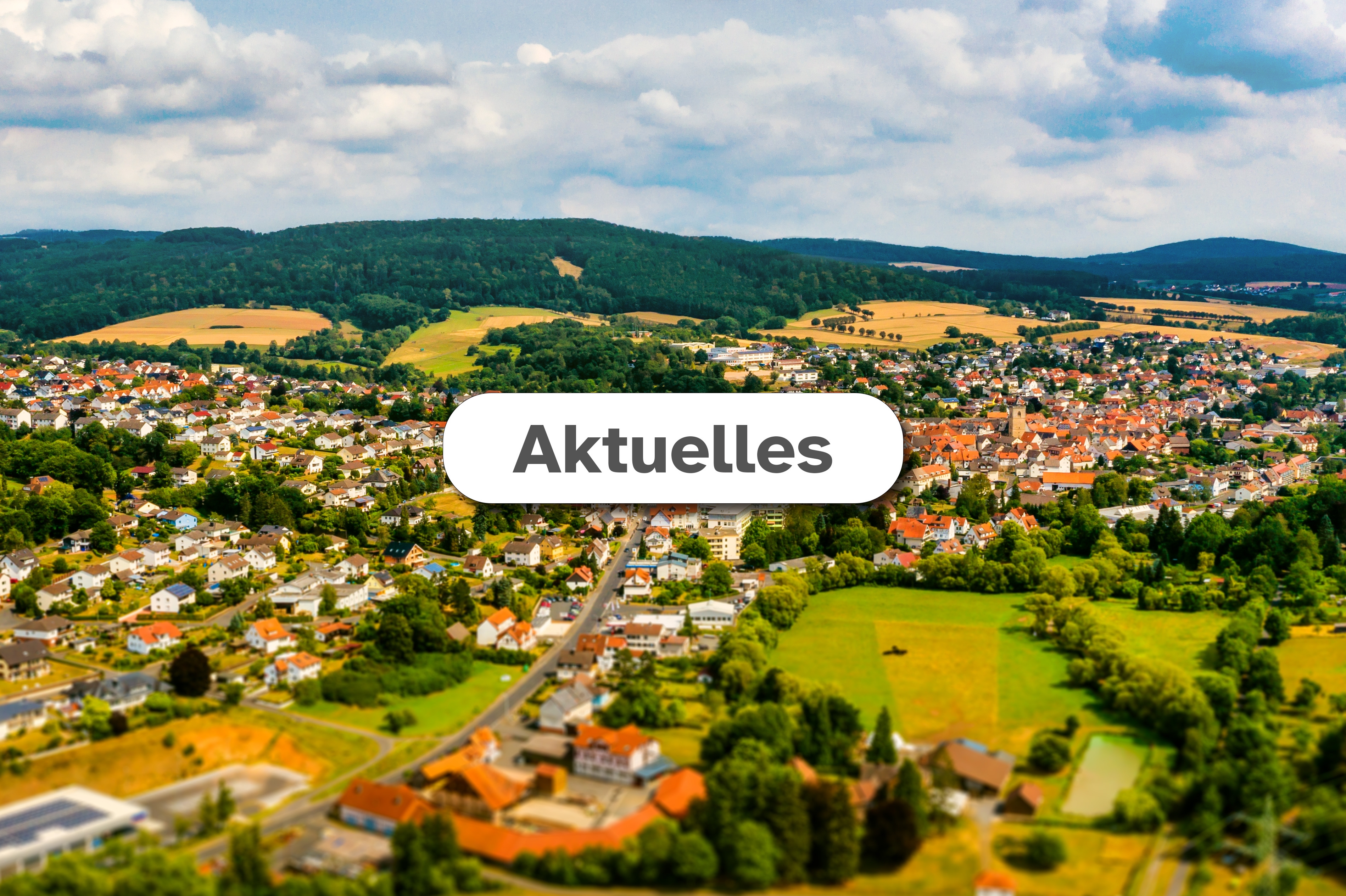 Neukirchen Aktuelles Luftaufnahme der Stadt Neukirchen im Hintergrund mit weißem Feld mittig in dem der Text "Aktuelles" zu lesen ist.