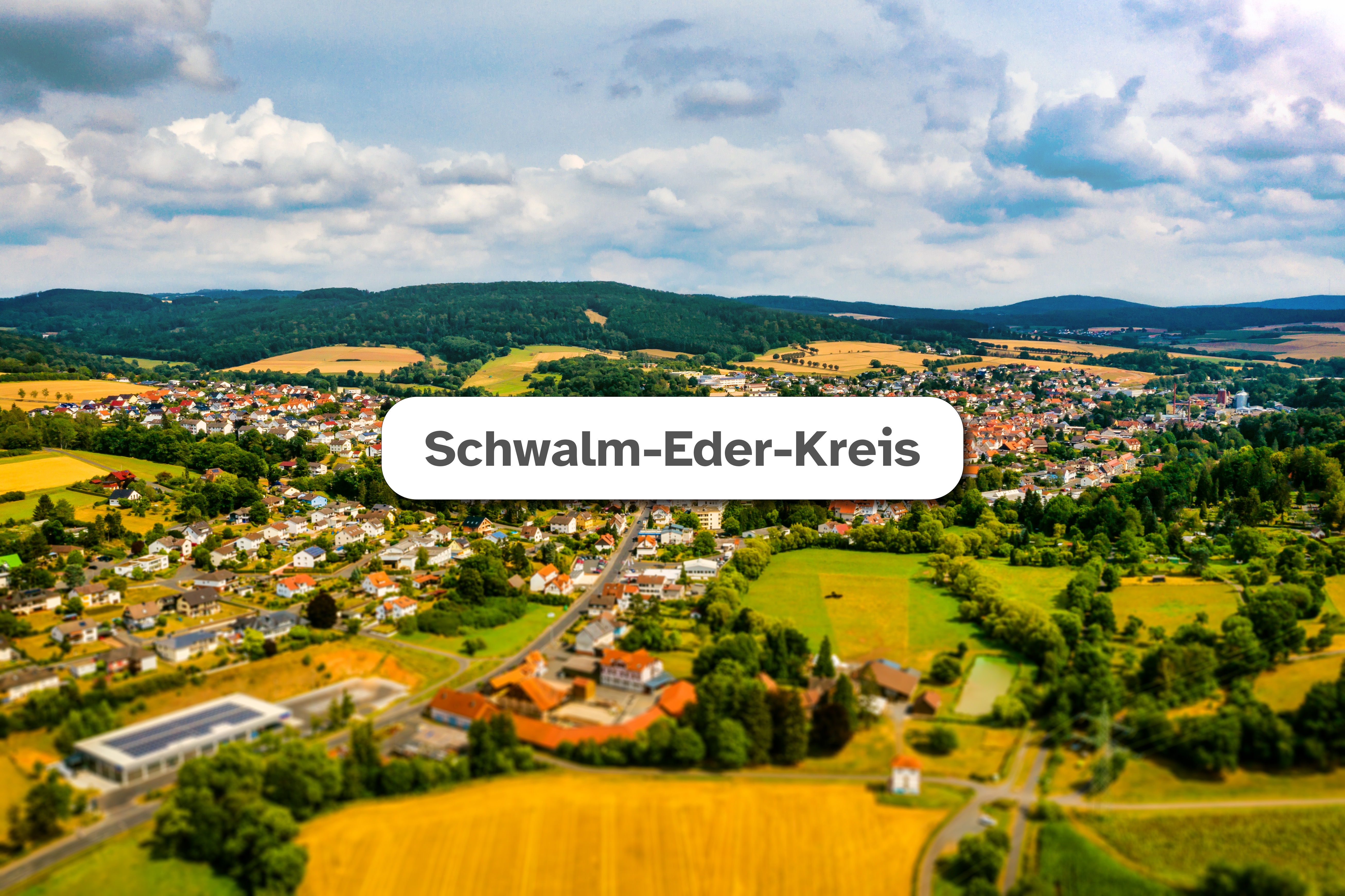 Neukirchen Aktuelles Schwalm-Eder-Kreis Luftaufnahme der Stadt Neukirchen im Hintergrund mit weißem Feld mittig in dem der Text "Schwalm-Eder-Kreis" zu lesen ist.